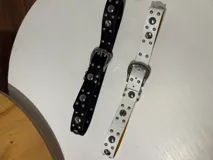 Cinto blanco de cuero sintético con tachas plateadas y hebilla metálica plateada.