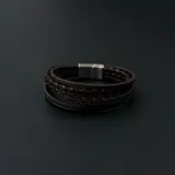 Pulsera multicapa para hombre compuesta por cuatro tiras de cuero marrón, incluyendo una trenzada y una lisa, con cierre magnético de acero inoxidable.