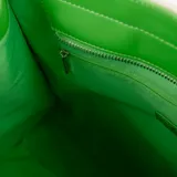 Bolso tipo tote de tela color crudo con detalles en cuero sintético verde. Tiene doble asa corta, correa larga regulable y extraíble, bolsillo frontal con cierre, cierre principal, bolsillo interno con cierre y dos bolsillos internos abiertos.