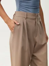 Pantalón de vestir color tostado de corte ancho y relajado, tiro alto con trabillas para cinturón, pinzas frontales y bolsillos laterales.