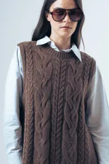 Chaleco de punto color marrón con diseño de ochos, cuello redondo y lazos laterales ajustables.