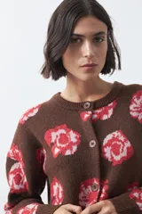 Cardigan de tejido jacquard color marrón con estampado floral en tonos rojo y rosado. Presenta cuello redondo, cierre frontal con botones y terminaciones acanaladas en puños y ruedo.