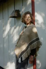 Poncho artesanal de lana en color beige, con diseño de tejido rústico y detalles de guardas geométricas en negro y blanco en los bordes. Presenta terminaciones con flecos largos en todo el contorno.