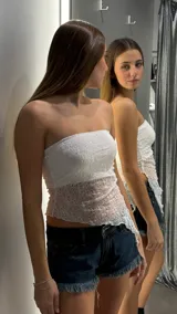 Top strapless de encaje blanco con diseño asimétrico en el ruedo, que presenta una capa superior de encaje semitransparente sobre una base ajustada.