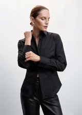 Camisa básica de algodón color negro, con cuello camisero, manga larga con puños abotonados y cierre frontal de botones.