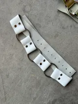 Cinturón blanco de cuero con argollas plateadas y hebilla ajustable.