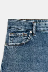 Jeans de tiro alto con corte barrel y diseño tapered, confeccionados en denim con efecto lavado y detalle de raya planchada. Presentan cintura con trabillas, cierre frontal con cremallera y botón, y bolsillos funcionales en delantero y espalda.