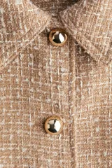 Chaqueta corta de tejido texturizado en color tostado, con cuello camisero, cierre frontal de botones metálicos dorados y diseño entallado con costuras moldeadoras.