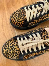 Sueco tipo zapatilla con diseño destalonado, confeccionado en cuero con estampado animal print de leopardo. Presenta cordones en tono beige y suela plana negra.