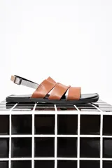 Sandalias chatas color marrón con tiras anchas de cuero y pulsera al tobillo con hebilla metálica.