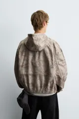 Cazadora negra de algodón con efecto lavado, corte relajado y capucha ajustable. Presenta cierre frontal de cremallera, bolsillos frontales tipo canguro y elásticos en puños y bajo.