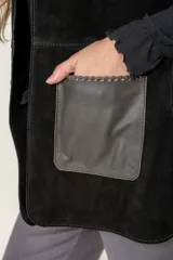 Chaleco de cuero negro con diseño sin mangas, corte recto y bolsillos frontales con contraste de textura. Presenta costuras visibles y un acabado artesanal.