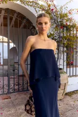 Vestido largo azul marino sin mangas, de corte recto con tajo lateral y diseño strapless con sobrecapa fluida superpuesta.