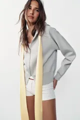 Chaqueta de punto con capucha, manga larga y cierre frontal con cremallera. Presenta un diseño de lazo decorativo en color amarillo en la zona del cuello.