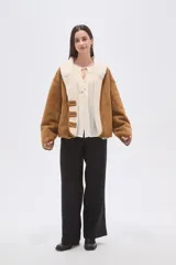 Chaqueta de gamuza sintética color camel con interior y cuello de corderito sintético color crema. Presenta un corte holgado, cierre frontal con botones y mangas largas.