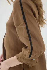 Blusa de lino color marrón, de corte recto y mangas 3/4. Presenta escote redondo con pequeños volados y pliegues frontales, además de detalles de encaje en las mangas y puños con volados.