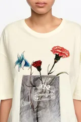 Remera negra de corte recto y holgado, confeccionada en algodón orgánico. Presenta cuello redondo, mangas cortas y estampa frontal de un ramo de flores en tonos coloridos con detalles artísticos.