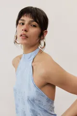 Top halter celeste con diseño asimétrico de corte más largo en la parte trasera, cuello alto y sutil estampado floral.