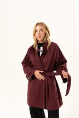 Trench de corte holgado color bordó, con cuello camisero, cierre frontal con botones y cinturón ajustable con hebilla. Presenta mangas largas con detalles de correas en los puños y bolsillos laterales.