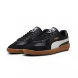 Championes Puma modelo Army Trainer, de diseño retro en color blanco con detalles en verde oscuro y suela de goma color caramelo. Presenta refuerzos de gamuza en la puntera y el logo de la marca en dorado en el lateral.