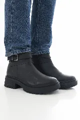 Botinetas de cuero negro con suela track y taco bajo. Presentan una correa decorativa con hebilla metálica alrededor del tobillo y cierre lateral interno.