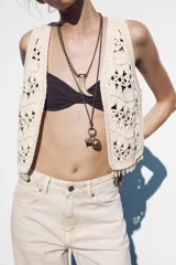 Chaleco abierto de punto color crudo con manga sisa y detalle de conchas en el ruedo.