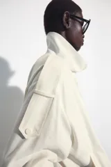 Chaqueta oversize negra confeccionada en hilatura con mezcla de modal, de corte fluido. Cuenta con cuello subido, manga larga con puños elásticos, bolsillos de vivo en el delantero y trabillas en los hombros. El bajo es abullonado con elástico y el cierre frontal es con botones a presión.