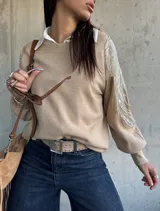 Sweater de punto color beige, con cuello redondo y mangas largas abullonadas. Presenta detalles bordados con lentejuelas y perlas en los hombros y parte superior de las mangas.