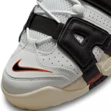 Championes Nike Air More Uptempo 96 de color blanco, negro y gris, con detalles en naranja y rojo. Presentan el característico diseño con las letras "AIR" sobredimensionadas en los laterales, suela de goma con amortiguación visible y un estilo urbano robusto.