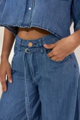 Pantalón de denim negro de tiro medio, corte wide leg con pierna muy ancha y caída fluida. Presenta un detalle de presilla metálica decorativa en la cintura.