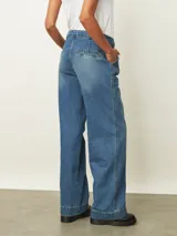 Jean de corte wide leg en color azul medio, con diseño de tiro alto y pinzas en la cintura. Presenta un estilo holgado y relajado con costuras reforzadas en el ruedo.