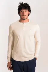 Remera manga larga de color beige con cuello redondo y cartera de botones frontal. Cuenta con puños ajustados y pequeño logo bordado en el pecho.