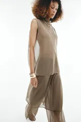Pantalón de punto fino color beige, de corte recto y holgado, con cintura elástica y una falda pareo superpuesta con nudo lateral.