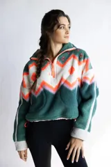 Buzo de polar con diseño estampado de estilo étnico en tonos verde, blanco y naranja. Presenta cuello alto con cierre frontal parcial, mangas largas con puños en contraste y cordón ajustable en el ruedo.