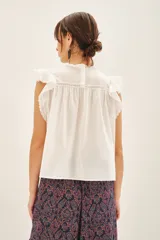 Camisa blanca de algodón con detalles de puntilla en el canesú, volados con terminación de puntillas en las mangas y cartera de botones en la parte superior de la espalda.