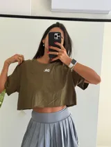Remera corta (crop top) de manga corta y cuello redondo, color verde militar, con un pequeño logo blanco bordado en el pecho.