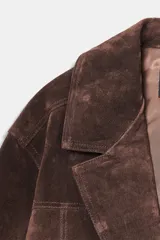 Chaqueta tipo blazer oversize de piel de ante color marrón oscuro, con cuello solapa de muescas, manga larga y bolsillos delanteros con solapa. Cierre frontal con botones.