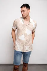 Camisa de manga corta con estampado de hojas en tonos beige y blanco, con cuello clásico y cierre frontal con botones.