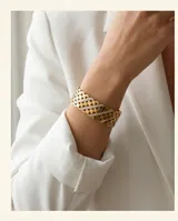 Pulsera tipo esclava rígida de acero con baño de oro, con diseño de malla calada y una línea central decorada con circonias brillantes.
