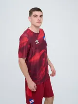 Remera de entrenamiento Umbro del Club Nacional de Football, modelo Press, para hombre. Diseño en tonos de rojo con patrón estampado tipo humo o abstracto, cuello redondo y mangas cortas. Incluye el logo de Umbro y el escudo del club en el pecho.