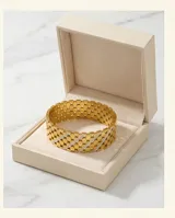 Pulsera tipo esclava rígida de acero con baño de oro, con diseño de malla calada y una línea central decorada con circonias brillantes.