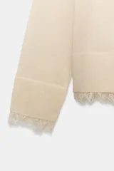 Jersey de cuello redondo y manga larga, confeccionado en tejido de punto fino. Presenta un diseño minimalista con un detalle de aplicación de encaje a tono en el bajo y en los puños.