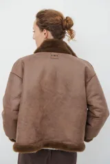 Chaqueta de piel sintética en color burdeos, con cuello alto y cierre frontal oculto. Presenta un diseño de corte recto y mangas largas con puños ligeramente ajustados.