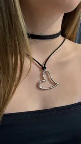 Gargantilla tipo choker compuesta por una cinta negra y un collar largo con dije de corazón plateado de contorno abierto.