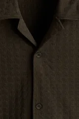 Camisa de manga corta H&M con cuello abierto, confeccionada en tejido de punto con textura. Presenta un diseño de corte holgado con bajo recto y aberturas laterales.