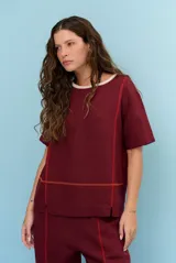 Blusa de lino color beige, de corte recto y mangas cortas, con costuras decorativas pespunteadas en tono rojizo que forman líneas verticales y horizontales.