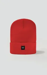 Gorro de tejido tipo beanie, color rojo, con borde doblado y un pequeño parche negro bordado con un símbolo de tijeras cruzadas en blanco.