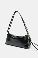 Bolso de hombro tipo baguette en color negro con acabado brillante. Presenta un diseño rectangular con cierre de cremallera superior y doble asa ajustable mediante hebillas metálicas.