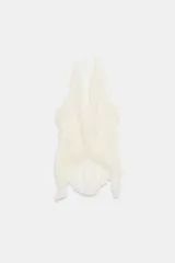 Top de encaje color blanco crudo, con cuello halter, escote en V profundo, volantes en los bordes y bajo asimétrico con lazada en el cuello.