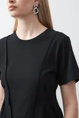 Remera de manga corta y cuello redondo, confeccionada en algodón. Presenta costuras verticales visibles en el frente que generan un efecto de entalle y estructura en la cintura.